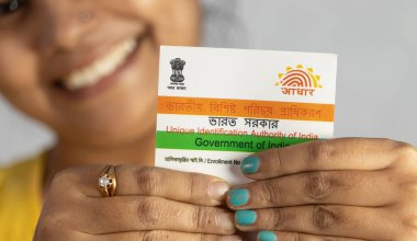 Birbhum, Batı Bengal / Hindistan - 21 Aralık 2021: Gülen yüzlü genç Hintli bir kadının elinde tuttuğu Aadhaar kartı üzerine seçici odaklanma