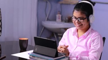 Pembe gömlekli Hintli kadın öğretmen evde tabletle konferans veriyor.