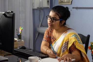 Evde bilgisayarla çalışan sari giyen Hintli kadın, ev konsepti üzerine çalışıyor.
