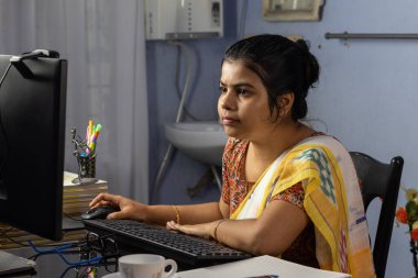 Evde bilgisayarla çalışan sari giyen Hintli kadın, ev konsepti üzerine çalışıyor.