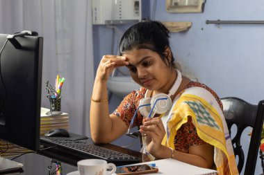 Sari giymiş Hintli bir kadın evden bilgisayarla çalışıyor ve baş ağrısı çekiyor, ev konseptinden çalışıyor.