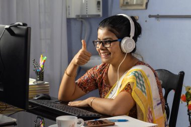 Sari giymiş Hintli bir kadın bilgisayarla çalışıyor ve evden internet üzerinden konuşuyor, online öğretim kavramı.