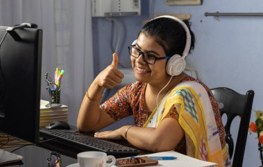 Sari giymiş Hintli bir kadın bilgisayarla çalışıyor ve evden internet üzerinden konuşuyor, online öğretim kavramı.
