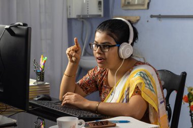 Sari giymiş Hintli bir kadın bilgisayarla çalışıyor ve evden internet üzerinden konuşuyor, online öğretim kavramı.