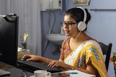 Sari giymiş Hintli bir kadın bilgisayarla çalışıyor ve evden internet üzerinden konuşuyor, online öğretim kavramı.