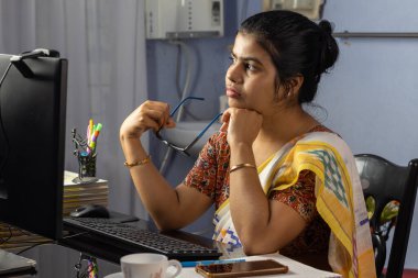 Evde bilgisayarla çalışan sari giyen Hintli kadın, ev konsepti üzerine çalışıyor.