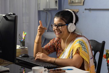 Sari giymiş Hintli bir kadın bilgisayarla çalışıyor ve evden internet üzerinden konuşuyor, online öğretim kavramı.