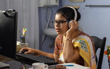 Sari giymiş Hintli bir kadın bilgisayarla çalışıyor ve evden internet üzerinden konuşuyor, online öğretim kavramı.