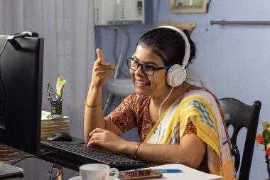 Sari giymiş Hintli bir kadın bilgisayarla çalışıyor ve evden internet üzerinden konuşuyor, online öğretim kavramı.
