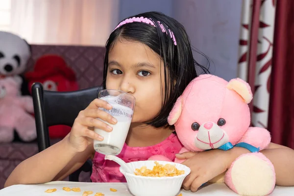 Hintli bir kız çocuğu mısır gevreğiyle süt içiyor ve kameraya bakıyor.