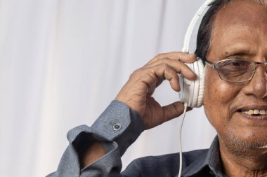 Yaşlı bir Hintlinin yakın plan fotoğrafı beyaz kulaklıkla müzik dinlemekten hoşlanıyor.