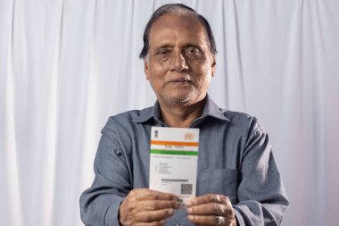 Beyaz arka planda elinde Aadhaar kartıyla gülümseyen Hintli yaşlı bir adam.