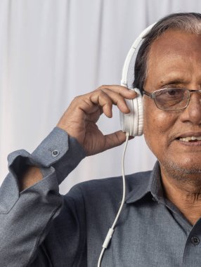 Yaşlı bir Hintlinin yakın plan fotoğrafı beyaz kulaklıkla müzik dinlemekten hoşlanıyor.