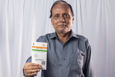 Beyaz arka planda elinde Aadhaar kartıyla gülümseyen Hintli yaşlı bir adam.