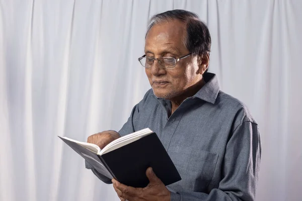 An old Indian man is reading books standing on white background