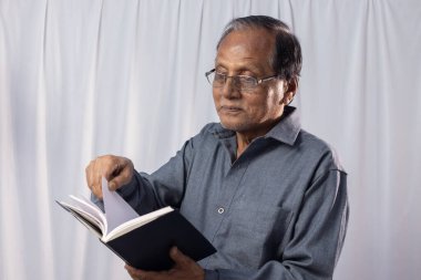 Yaşlı bir Hintli beyaz arka planda kitap okuyor.