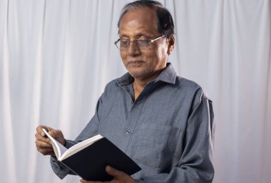 Yaşlı bir Hintli beyaz arka planda kitap okuyor.