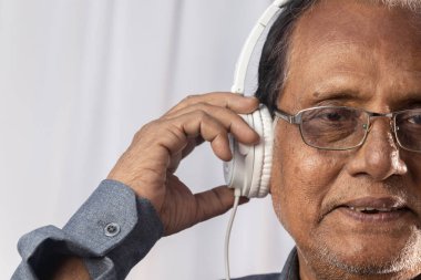 Yaşlı bir Hintlinin yakın plan fotoğrafı beyaz kulaklıkla müzik dinlemekten hoşlanıyor.