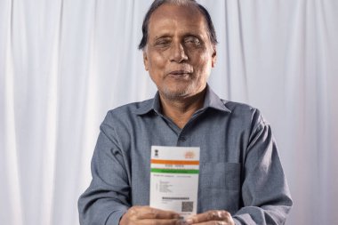 Beyaz arka planda elinde Aadhaar kartıyla gülümseyen Hintli yaşlı bir adam.