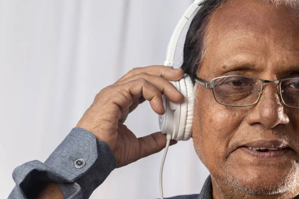 Yaşlı bir Hintlinin yakın plan fotoğrafı beyaz kulaklıkla müzik dinlemekten hoşlanıyor.
