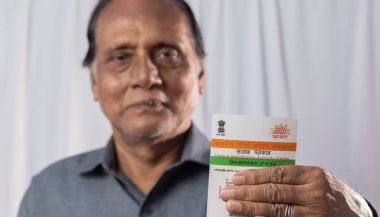 Birbhum, Batı Bengal / Hindistan - 15 Mart 2022: Gülen suratlı yaşlı bir Hintli adamın elinde tuttuğu Aadhaar kartı üzerine seçici odaklanma