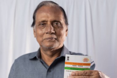 Birbhum, Batı Bengal / Hindistan - 15 Mart 2022: Gülen suratlı yaşlı bir Hintli adamın elinde tuttuğu Aadhaar kartı üzerine seçici odaklanma