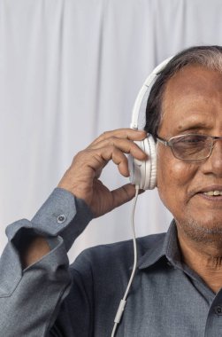 Yaşlı bir Hintlinin yakın plan fotoğrafı beyaz kulaklıkla müzik dinlemekten hoşlanıyor.