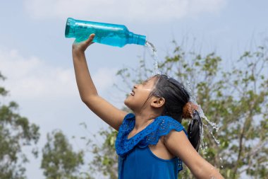 Hintli bir kız yazın serinlemek için gökyüzünün altındaki mavi plastik bir şişeden kafasına su döktü.