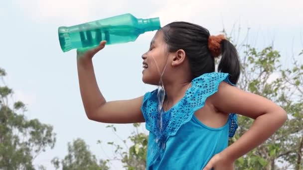 青空の下で青いペットボトルから頭の上に水を注ぐインドの女の子は夏に冷却するために — ストック動画