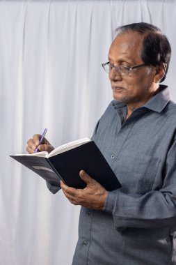 Yaşlı bir Hintli beyaz arka planda durup notlar alıyor.