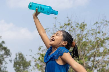 Hintli bir kız yazın serinlemek için gökyüzünün altındaki mavi plastik bir şişeden kafasına su döktü.