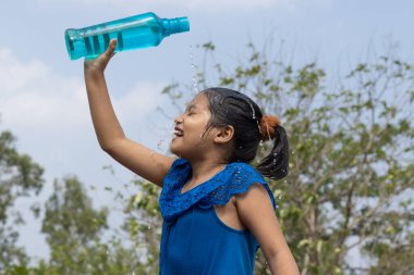 Hintli bir kız yazın serinlemek için gökyüzünün altındaki mavi plastik bir şişeden kafasına su döktü.