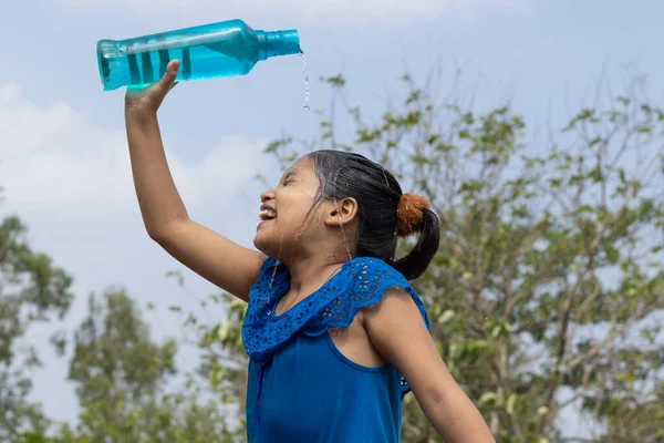 Hintli bir kız yazın serinlemek için gökyüzünün altındaki mavi plastik bir şişeden kafasına su döktü.