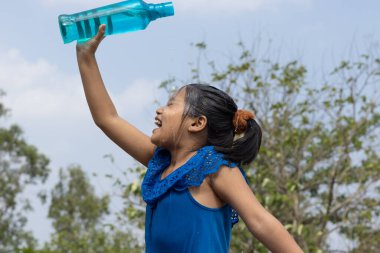 Hintli bir kız yazın serinlemek için gökyüzünün altındaki mavi plastik bir şişeden kafasına su döktü.