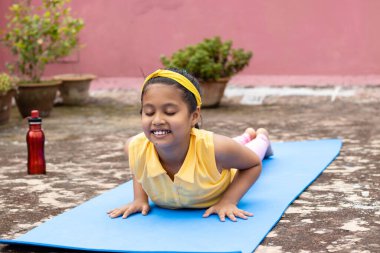 An Indian girl child practicing yoga in smiling face on yoga mat outdoors