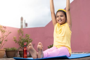 An Indian girl child practicing yoga in smiling face on yoga mat outdoors