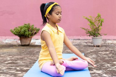 An Indian girl child practicing yoga on yoga mat outdoors