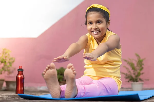 An Indian girl child practicing yoga in smiling face on yoga mat outdoors