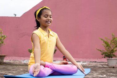 An Indian girl child practicing yoga in smiling face on yoga mat outdoors