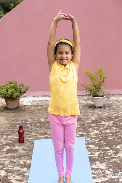 An Indian girl child practicing yoga in smiling face on yoga mat outdoors