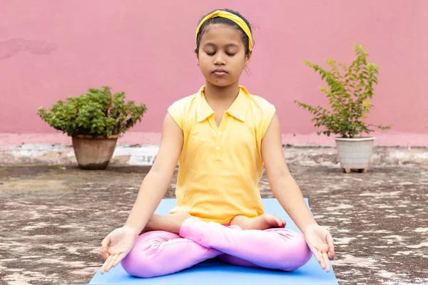 An Indian girl child practicing yoga on yoga mat outdoors