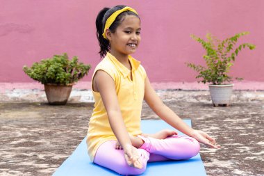 An Indian girl child practicing yoga in smiling face on yoga mat outdoors