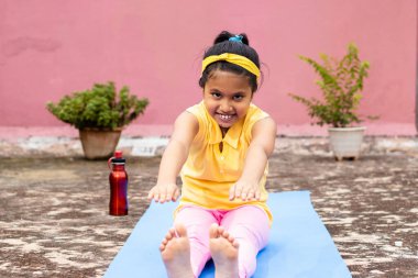 An Indian girl child practicing yoga in smiling face on yoga mat outdoors
