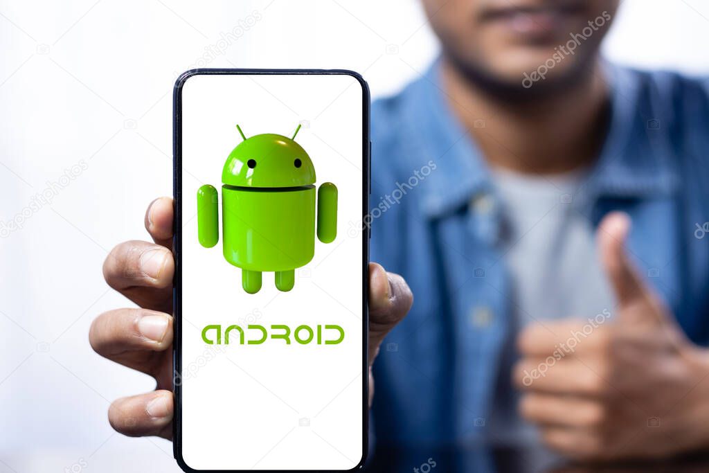 Close up of a smart phone screen with android logo held in hand by an Indian smiling male