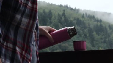 Breakfast. Female hands pour coffee from a thermos. Concept of comfort and cozy. Traveler Enjoying Hot Tea In Mug On Forest Adventure. Weather in mountains. Misty fog blowing over pine tree forest.