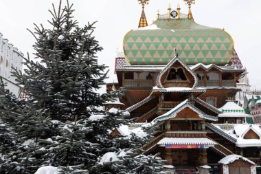 Old slavic style wooden orthodox church made of massive logs. The building covered and surrounded by winter white snow. The large wooden cross on the top of the sanctuary. Snowy blue fir stands beside