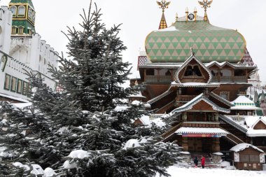 Old slavic style wooden orthodox church made of massive logs. The building covered and surrounded by winter white snow. The large wooden cross on the top of the sanctuary. Snowy blue fir stands beside
