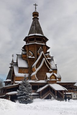 Old slavic style wooden orthodox church made of massive logs. The building covered and surrounded by winter white snow. The large wooden cross on the top of the sanctuary. Snowy blue fir stands beside