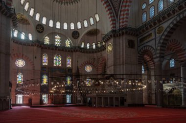 Istanbul, Turkey - 1 March 2021. Rich interior of the Suleymaniye mosque in Istanbul. Bright luminous windows with mosaics and a lot of glass candles lanterns hang on huge chandeliers. 