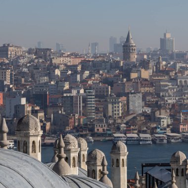 Panoramic urban cityscape of Istanbul from the rooftop of Suleymaniye Mosque. There are visible domes and chimneys of the mosque; Galata tower, Karakoy district, Golden Horn strait and sea transport.